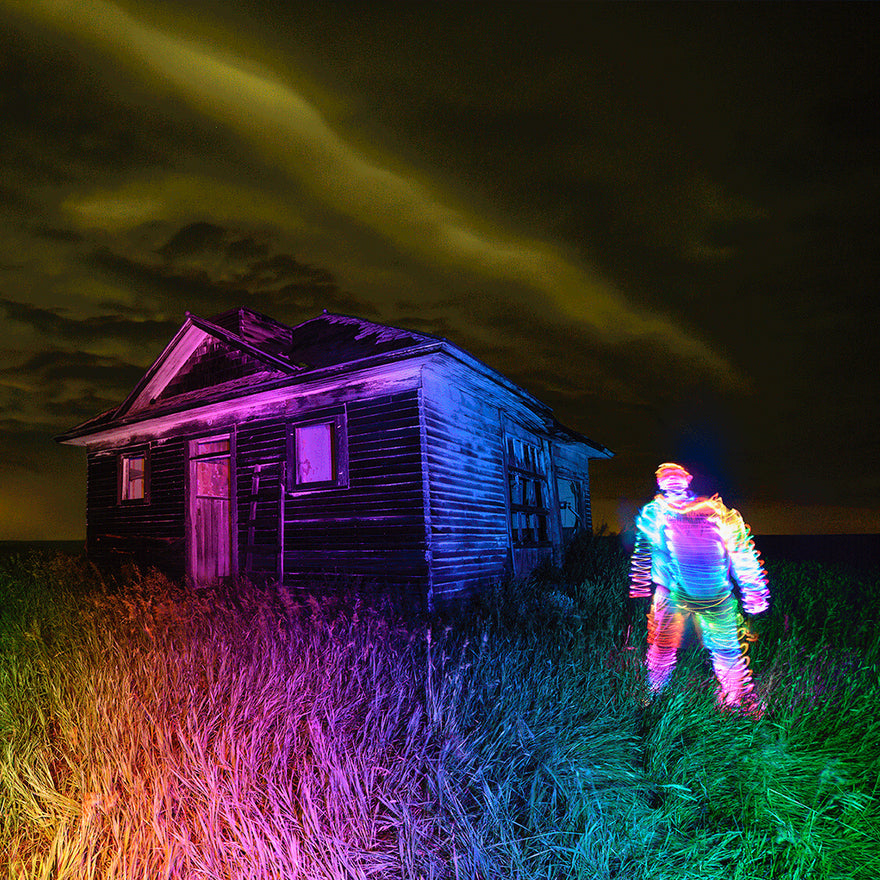 Colorful light painting created with an Acrylic Writer near an abandoned cabin on farmland, with bright scribbles outlining a subject and the cabin illuminated in vivid hues