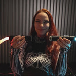 A woman connects two white BitWhips back to back using RGB Critter BT flashlights, forming a Double BitWhip for festival flow arts performances.