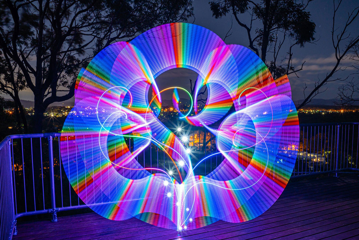 Rainbow saber light painting on a lookout above a city at night