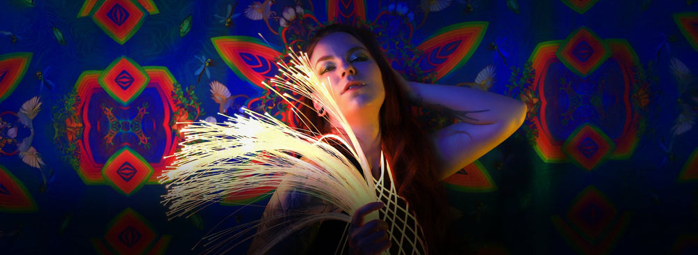 Performer holding a glowing fiber optic whip in front of a kaleidoscopic backdrop