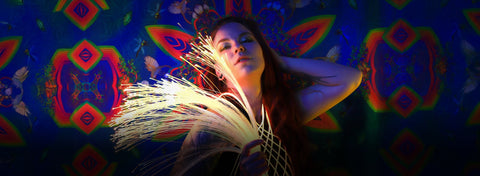 Performer holding a glowing fiber optic whip in front of a kaleidoscopic backdrop