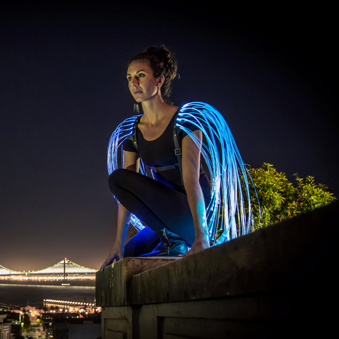 Woman with fiber optic wings is sitting on a building.