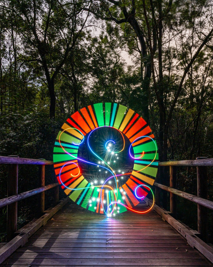 Long exposure light painting by Stephen Knight: a tube spun into a rainbow orb on a footbridge
