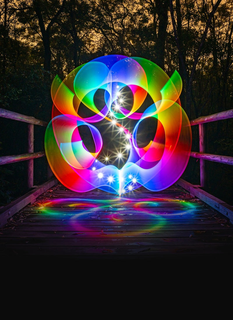 Long-exposure light painting: a rainbow orb of light drawn on a wooden footbridge at dusk