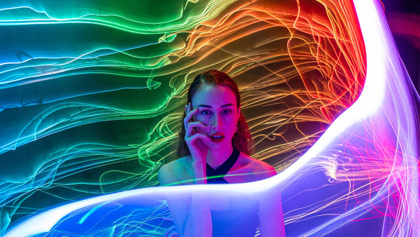 Fiber optic whip light trails arcing around a seated performer, long exposure light painting