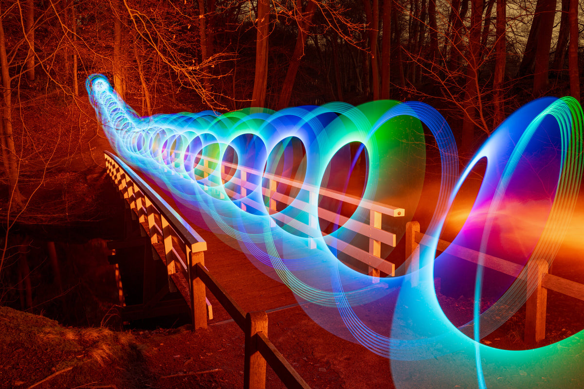 Rainbow light rings along a wooden bridge at night, by Hugo Baptista